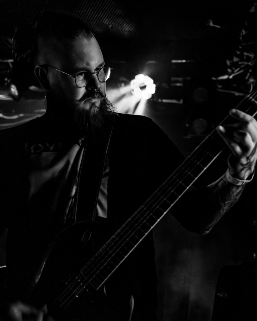 A musician playing an electric guitar on stage, with dramatic lighting illuminating the scene, creating a moody black and white effect.