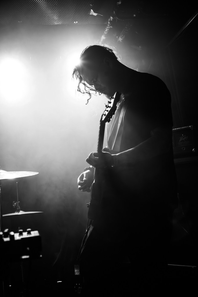 A silhouetted guitarist performing on stage, surrounded by smoke and bright lights, creating a dramatic atmosphere.
