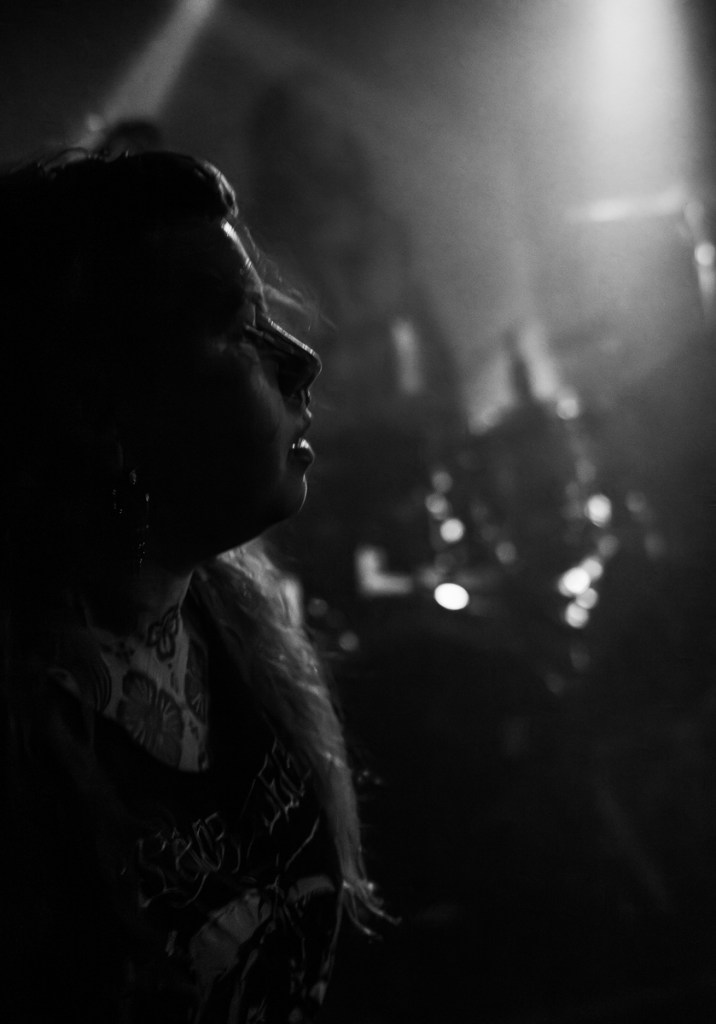 Profile of a person with long hair and tattoos, illuminated by dim stage lights in a concert setting.